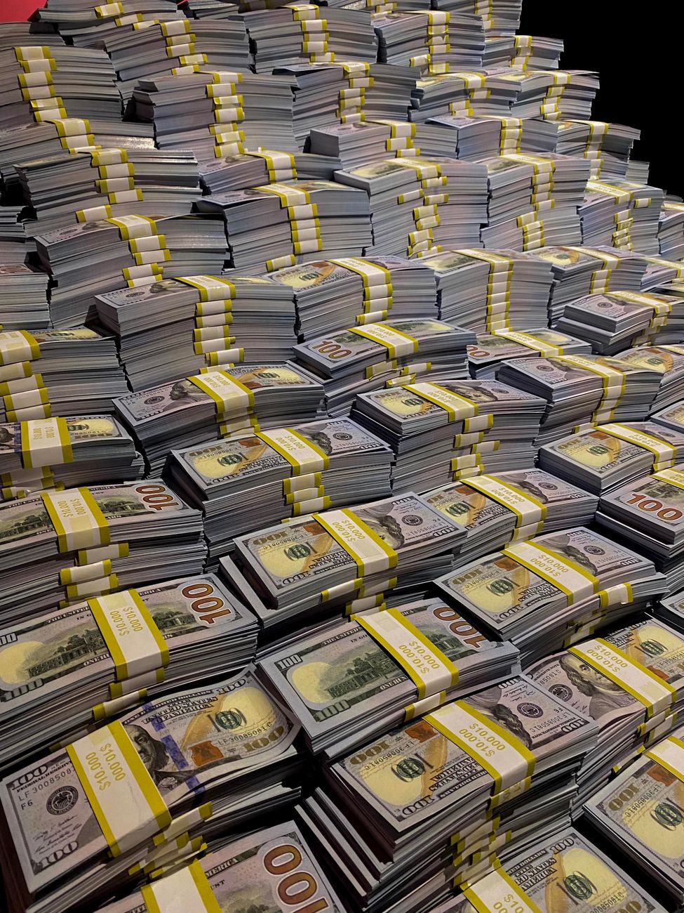 A large pile of neatly stacked bundles of U.S. currency, featuring multiple stacks labeled with yellow bands indicating denominations.